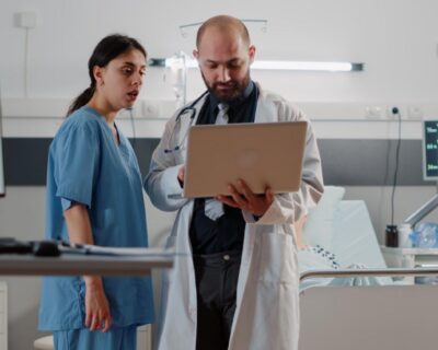 doctor-doing-consultation-with-retired-patient-bed-medic-with-laptop-talking-nurse-about-healthcare-medicine-before-examining-patient-with-nasal-oxygen-tube-heart-rate-monitor-1